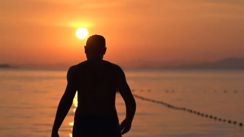 Man silhouette walking on tropical beach at sunset in super slow motion