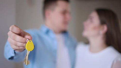 Closeup New Flat Key with Blurred Happy Young Couple Talking at Background Smiling