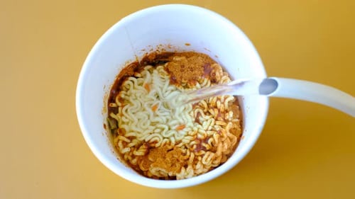 Water is poured into a box with instant noodles on yellow background top view.