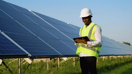 Afroamerikanischer Ingenieur nutzt digitales Tablet, um Solarzellenpaneele zu warten, Techniker bei der Arbeit