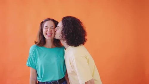 Man Kissing Laughing Woman on Orange Background