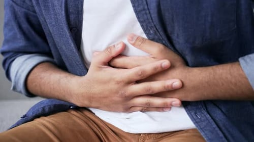 Close up. Male hands holding massaging stomach. Man in white shirt feels stomach pain sitting