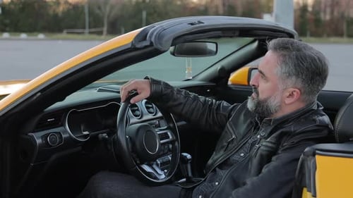 A Confident Man is Sitting in a Yellow Sports Car Mature Man with Gray Beard Relaxing in a Parked