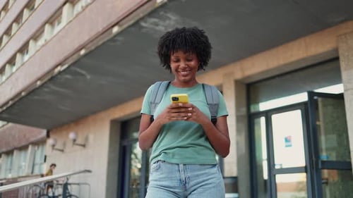 Young student engaging with smartphone while walking on campus