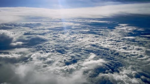 View through window on wing of commercial plane flying above white bright clouds