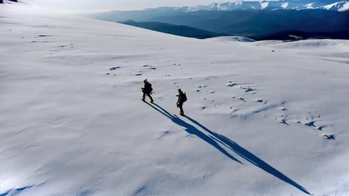 Drone shot of two hikers climbing up a snow-covered mountain peak.