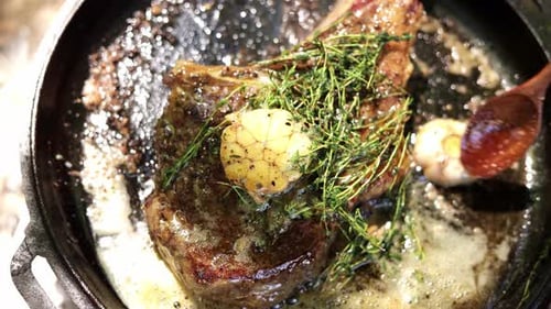 Steak sizzles in pan with butter and herbs