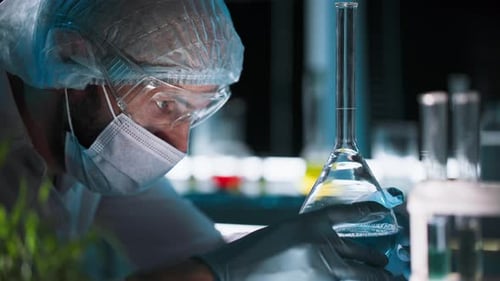 Männlicher Labortechniker in Schutzkleidung forscht mit Chemikalien in einer Flasche in einem