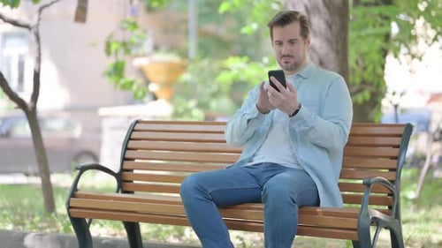 Man Using Smartphone on Park Bench During Daytime