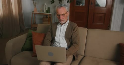 Senior Man Using Laptop on Couch at Home