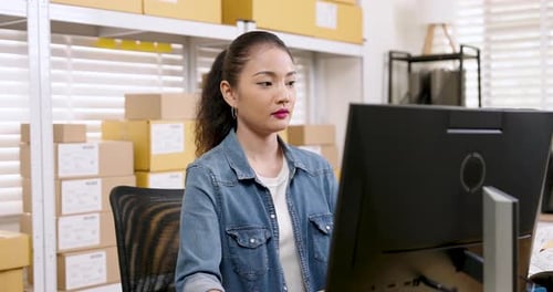 Woman Working at Computer in Office with Boxes