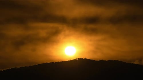 Time lapse of the sun setting over hills that are covered with clouds.