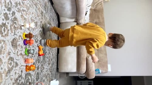 Hübscher kaukasischer Junge im gelben Anzug legte Spielzeugtiere auf den Boden.