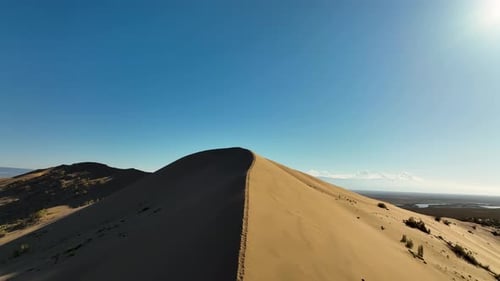 Lone figure on a desert dune overlooking a lake and mountains