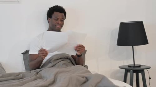Man Reading Paper in Bed at Home