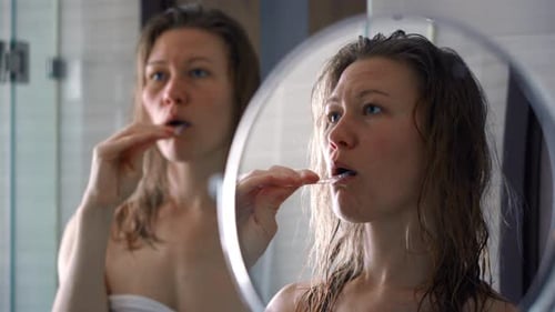 Woman Brushing Teeth in Bathroom Mirror