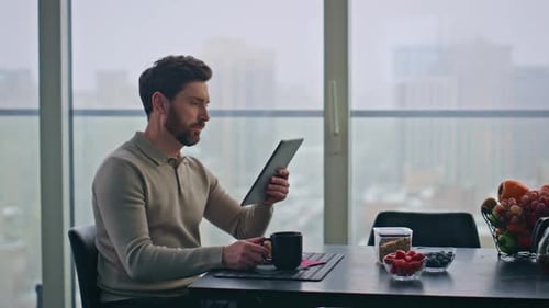 Blurred Man Reading Tablet Sitting Panoramic Kitchen Table at Morning Closeup