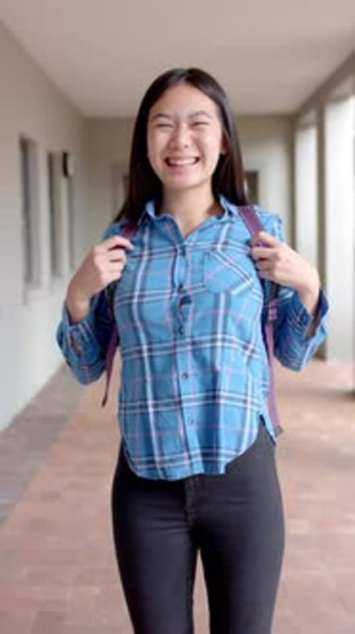 Vídeo vertical: En la escuela secundaria, una estudiante asiática con camisa azul a cuadros se ríe