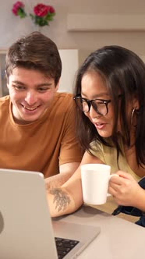 Young Couple Laughing Together While Using Laptop Indoors