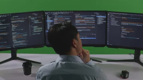 Asian Man Thinking About Something While Write Code With Multiple Computer Screens In Green Screen