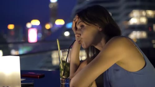 Lonely young woman sits on a rooftop terrace drinking wine and thinking of her troubles