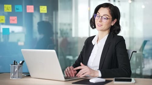 Professionelle Frau im Geschäftsoutfit am Schreibtisch, die mit einem Laptop einen Videoanruf führt.