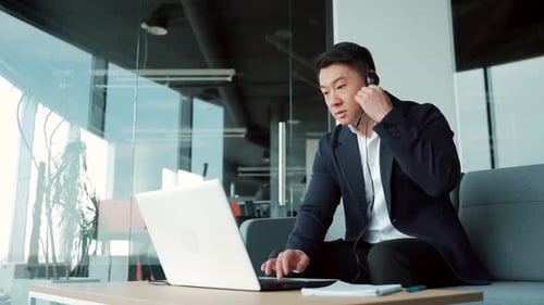 Man Works at Laptop with Headset in Office