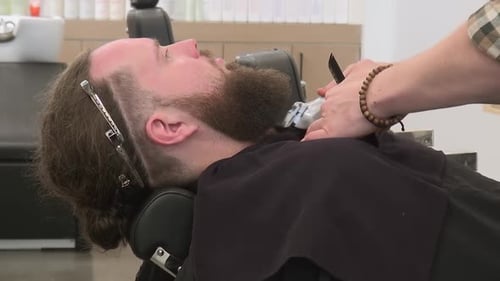 Trimmer used to shape jaw line of man's hipster beard in barber shop