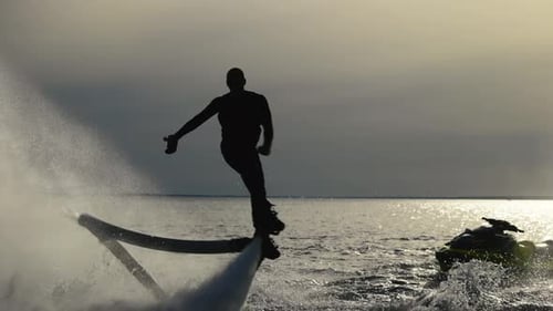Water Extreme Flyboarder führt Tricks über dem Wasser durch die Silhouette eines nicht wiederzuerkennenden männlichen Flyboarders