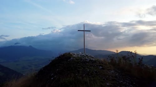 Aerial View of a Religious Christian Steel Cross on a Hill in the Mountainous Countryside in Sunset