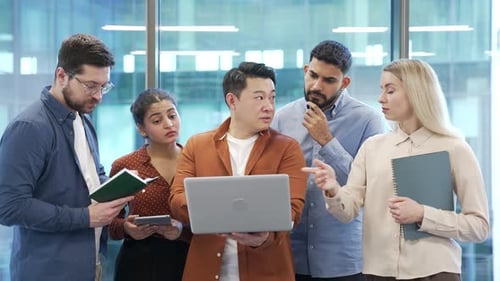 Male manager explains work issue to group of subordinate workers using laptop in business office.