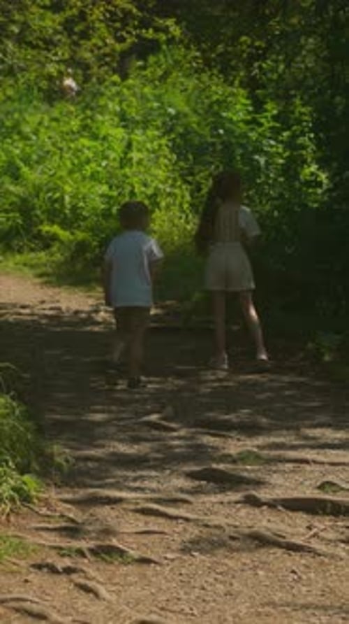 Little Brother and Sister Stand on Shaded Path in Forest