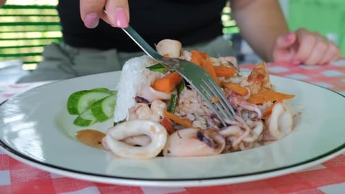 Mujer comiendo mariscos salteados con arroz en un café