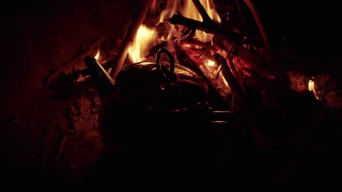 A blackened metal kettle nestled among burning wood and branches,