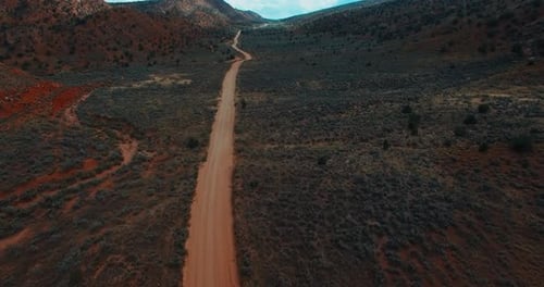 Dramatic aerial forward tilt up over dirt road leading through empty savanna
