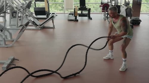 Man Performing Battle Ropes Workout in Modern Gym