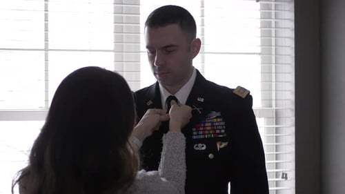 Woman Adjusts Necktie of Man in Military Uniform