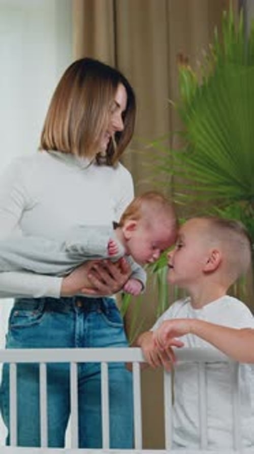 Mother holding baby with child near crib indoor