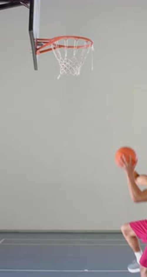 Vidéo verticale : en train de sauter au dunk basketball, un athlète masculin en tenue de sport atteignant un cerceau