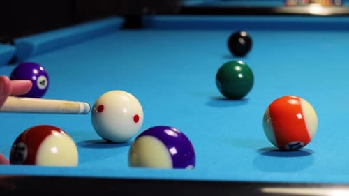 Hitting white ball against green ball in a game of pool billiards.