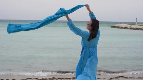 Woman Having Fun While Waving Blue Scarf on Seashore at Beach
