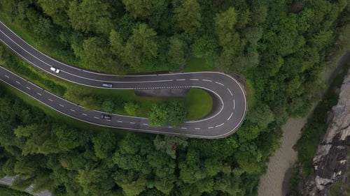 Cars Driving on Winding Mountain Road Surrounded By Lush Green Forest