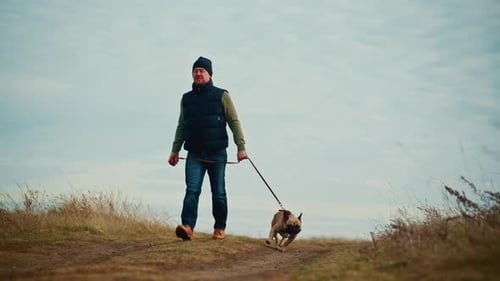 Un hombre disfruta de un tranquilo paseo con su juguetón perro por un sendero pintoresco rodeado de naturaleza y abierto
