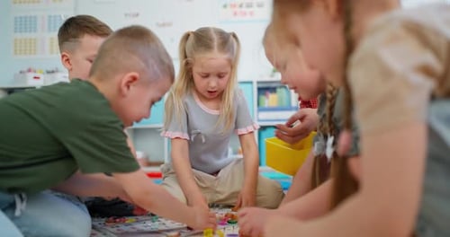 Young Children and Teacher Sitting on Classroom Floor Playing a Colorful Educational Board Game