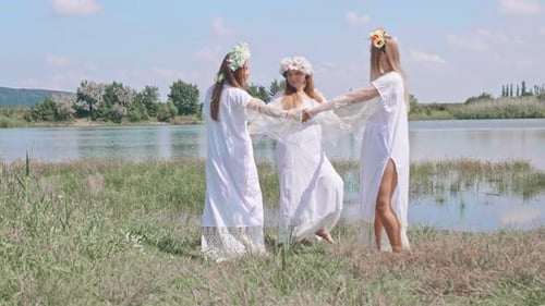 Women in White Dresses Holding Hands near Lake