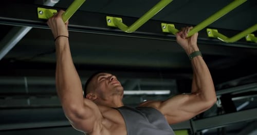 Starker Mann macht Klimmzüge in einem modernen Fitnessstudio und demonstriert Stärke