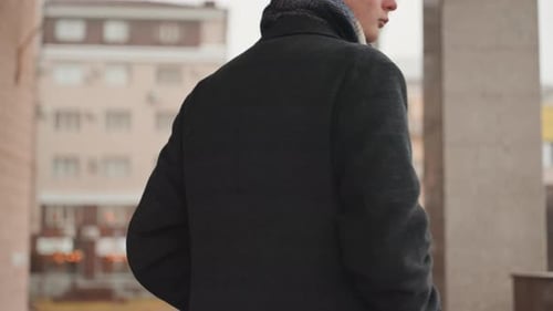 Man with cap and coat walks along city sidewalk