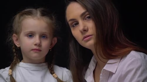 Young Mother Sitting with Her Daughter Both with Serious Expressions