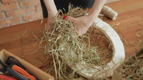 Decorator Shaping Dried Hay on Circular Base Using Hands with Red Nails