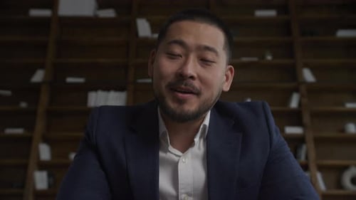 Man in Suit Speaking in front of Bookshelf